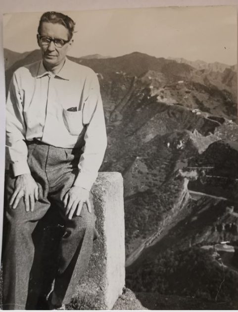 Valokuva Aarne Haapakoskesta istumassa muurilla ja takana vuorenhuippujono